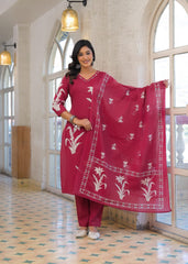 A woman models a traditional Indian salwar kameez suit in a bright indoor setting with arched windows. The set is a deep magenta pink with white floral embroidery, including a matching dupatta.