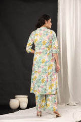 A woman stands with her back to the camera wearing a long-sleeved floral printed kurta and matching pants. The outfit features a multicolor floral pattern on a light cream base.