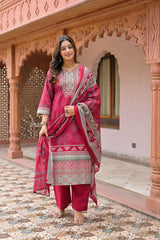 A woman models a traditional Indian salwar kameez suit set in a pink courtyard. The set includes a magenta-pink kurta with intricate multicolor embroidery, matching pink trousers, and a coordinating pink dupatta with a gray and gold border.