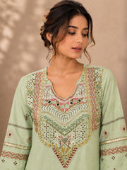 A woman wearing a light sage green embroidered kurta with intricate multicolor detailing on the neckline and sleeves, set against a soft beige background.