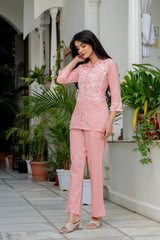 Woman in a pink outfit standing in front of a building with plants.