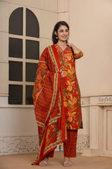 A woman models a traditional red and orange printed salwar kameez suit with a matching dupatta in front of a beige stone wall with an arched window.