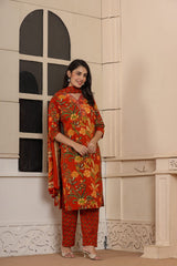 A woman modeling a red and orange floral printed salwar kameez suit with matching patterned pants, standing in front of a cream-colored wall with a decorative arched window.