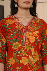 A close-up of a woman wearing a rust-orange cotton kurta with a vibrant yellow, orange, and green floral print and embroidered details on the V-neckline.