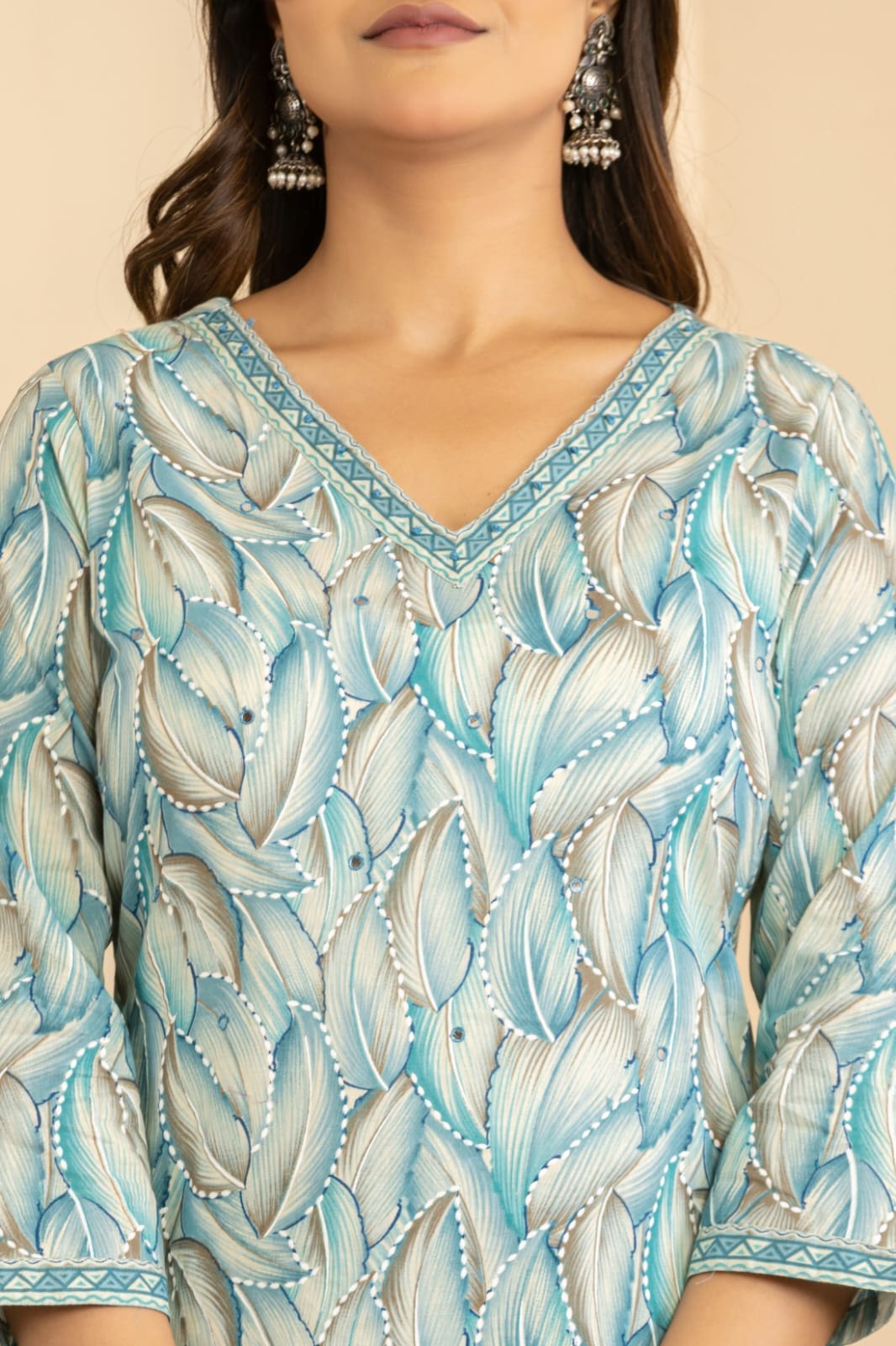 A close-up of a woman wearing a light blue and white patterned V-neck top with three-quarter sleeves and matching patterned borders.