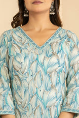 A close-up of a woman wearing a light blue and white patterned V-neck top with three-quarter sleeves and matching patterned borders.