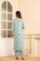 A woman stands with her back to the camera wearing a light blue and white patterned kurta with matching striped pants, standing in front of a cream-colored wall with a window.