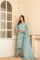 A woman models a light blue and white printed ethnic suit set consisting of a kurta, trouser pants, and a dupatta, standing in a cream-colored interior setting.